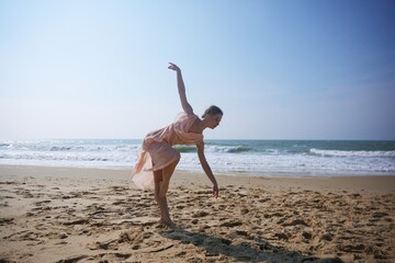 Dancer in mid-motion balancing pose on sandy beach with ocean waves behind