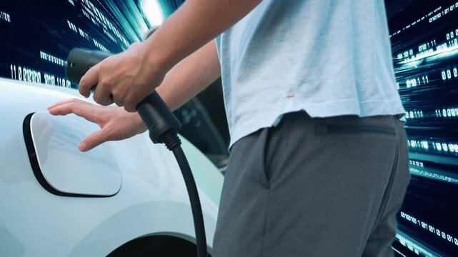 Progressive man charge electric car with power cable plug from charging station with technology background of binary code flying through votex. EV car concept with modern technology.