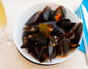 Portion of steamed mussels served with bay leaf on white plate. Spanish dish mejillon la marinera