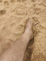 Human leg partially buried in light beach sand with a natural and wet texture