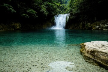 Naklejka premium Embracing nature’s serenity at a tranquil turquoise waterfall surrounded by lush green foliage Generative AI