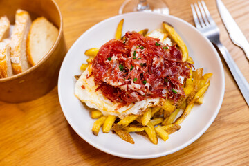 Huevos estrellados with potatoes and hamon on plate with fork knife and glass of wine and some bread