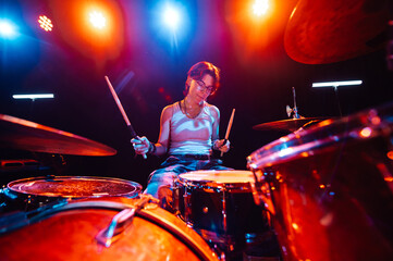 Female drummer performing energetically on stage under colorful lights