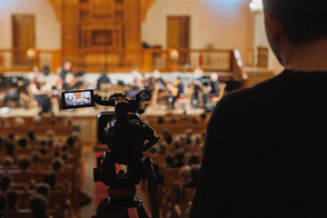 A man is capturing a photograph of an orchestra performance using his camera device, aiming to...