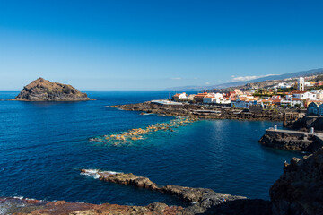 Fototapeta premium Coastal view of Garachico with the volcanic rock islet Roque de Garachico, Tenerife, Canary Islands, Spain, overlooking the Atlantic Ocean under a clear blue sky