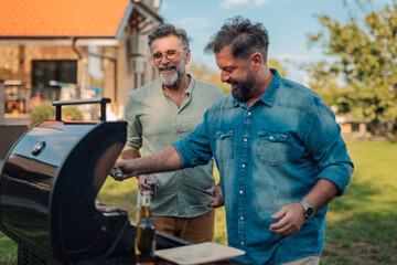 Two happy men preparing barbecue in the backyard of their house