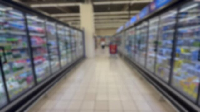 A blurry, out‑of‑focus view of a standard supermarket aisle lined with shelves of household and grocery items.