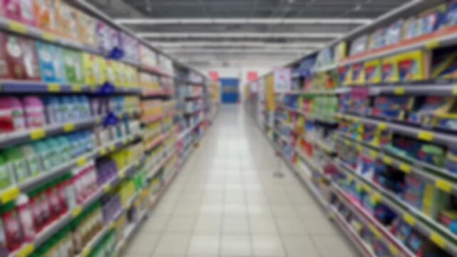A blurry, out‑of‑focus view of a standard supermarket aisle lined with shelves of household and grocery items.