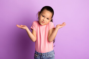 I Don't Know. Portrait of confused child shrugging shoulders with spreaded hands over purple...