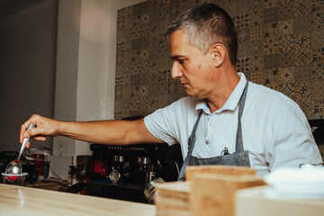photo of colombian senior latino barista preparing cherry drink in colombian coffee shop