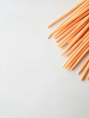 Fototapeta premium Bunch of orange-colored straws arranged in a diagonal line on a white background. the straws appear to be fresh and uncooked, with a smooth texture and a shiny surface.