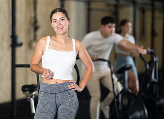 Fototapeta premium Young athletic woman posing by exercise bike in gym..