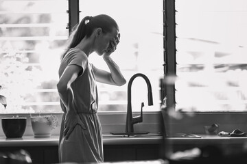Middle aged woman experiencing stress depression mental pain, at home near kitchen window
