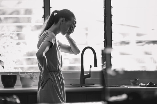 Middle aged woman experiencing stress depression mental pain, at home near kitchen window
