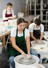 Young woman sculpting ceramic product on potter's wheel in workshop