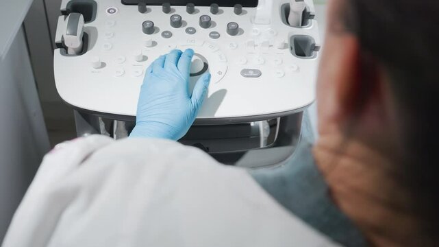 Medical radiation technologist wearing lab gloves operates body scanner by adjusting settings and pressing control buttons on diagnostic machine during patient examination in clinical environment