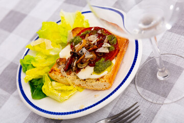 Hot sandwich on toasted baguette with mayonnaise, baked tomatoes, mushrooms, onions, chorizo sausage and grated parmesan cheese seasoned with fragrant basil sauce served on plate with fresh lettuce..