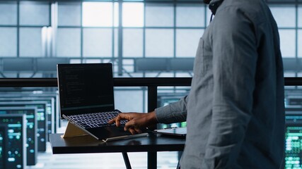Technician in data center using AI on laptop and tablet, developing disaster recovery plans. Server...