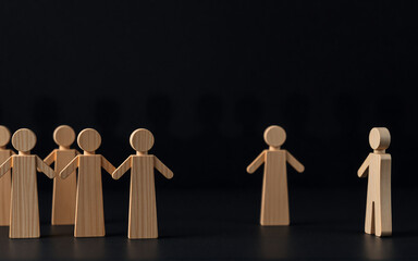 Wooden figures confront each other in a dark studio setting. A group faces a single figure, suggesting division, disagreement, or opposition.