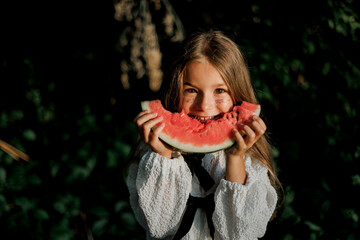 stylish little girl eating a juicy watermelon during a children's picnic in the evening in nature