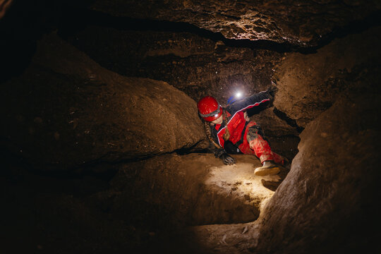 A 6-year-old girl in a protective suit and helmet with a flashlight in the middle of a natural underground cave is walking the tourist route of a caver - Powered by Adobe