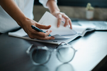 Close-up of hands writing on documents at a desk with glasses, showcasing a professional office...