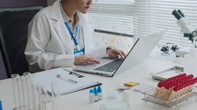 High qualified female scientist working on laptop and writing down experimental data in light lab