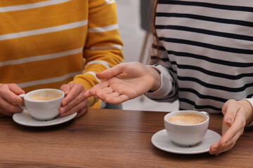 Coffee break. Women with cups of hot drinks at wooden table indoors, closeup