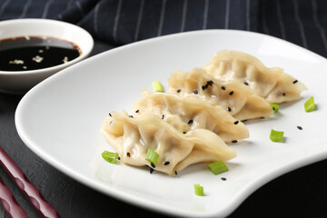 Delicious gyoza dumplings with chives and sesame seeds served on black table, closeup