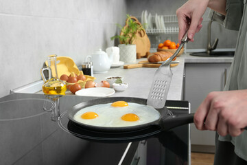 Woman cooking eggs in frying pan on cooktop indoors, closeup
