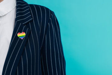 Woman with heart shaped pin in LGBT colors on light blue background, closeup. Space for text