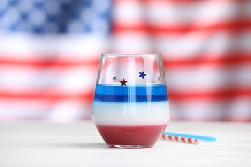 Tasty cocktail in glass and straws on white wooden table against flag of USA