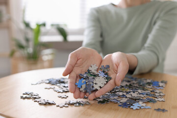 Woman solving puzzle at wooden table indoors, closeup. Space for text
