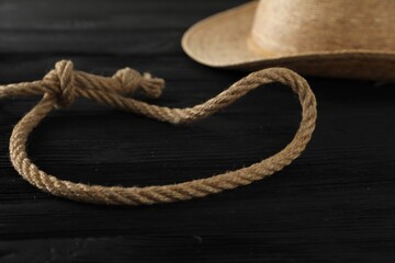 Lasso made of cotton rope and straw hat on black wooden background, closeup