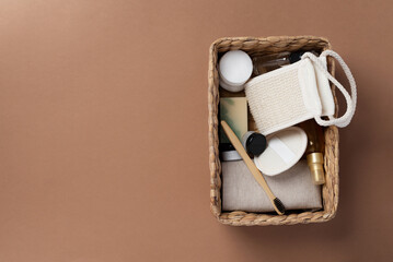 Top view of bathroom tools and organic cosmetic products in woven basket on brown background emphasizing natural, eco-friendly beauty essentials and self-care routine concept