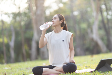 A enthusiastic Asian sports woman stopped after exercising at the garden, sitting on a exercise...