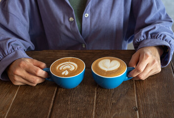 Cropped shot view of woman with a couple cup of hot Cappuccino coffee. The taste of cappuccinos can be described as creamy, smooth, and balanced.