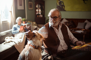Senior man in wheelchair painting with dog beside him in cozy living room studio