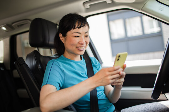 Smiling Asian woman texting on smartphone wearing sport clothes inside a car