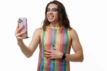 Genderqueer person takes a selfie wearing pride clothing, smiling and posing happily for the camera.