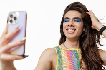 Genderqueer person takes a selfie wearing pride clothing, smiling and posing happily for the camera.