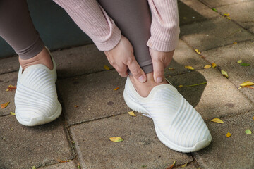 Woman Massaging Sore Ankle While Sitting Outdoor Wearing Gray Leggings and White Shoes with...
