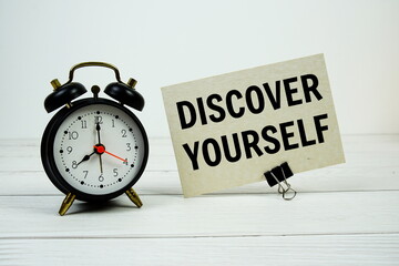 Discover Yourself text on paper card with alarm clock on wooden background