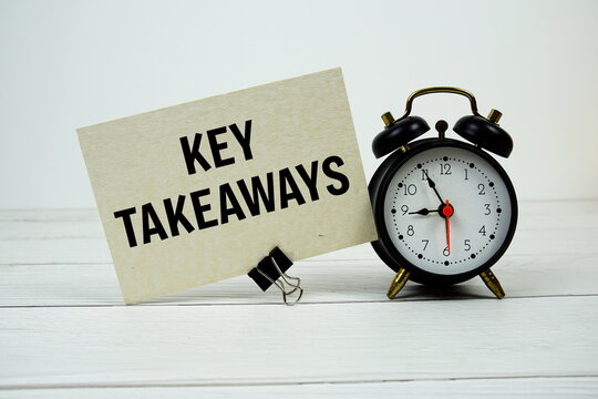 Key takeaways text on paper card with alarm clock on wooden background