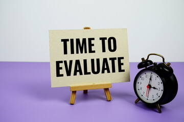 Time to Evaluate text on paper card with alarm clock on purple background