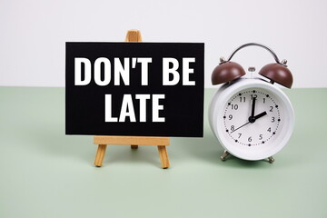Don't Be Late text on paper card with alarm clock on green background