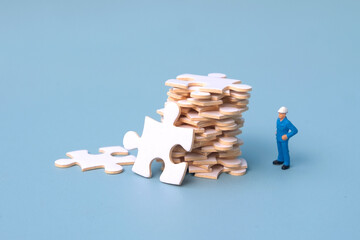 Miniature people with jigsaw puzzles piled up in front of theman. employee is looking at the pile...