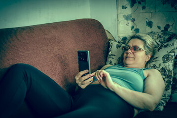 A woman is laying on a couch and using her cell phone