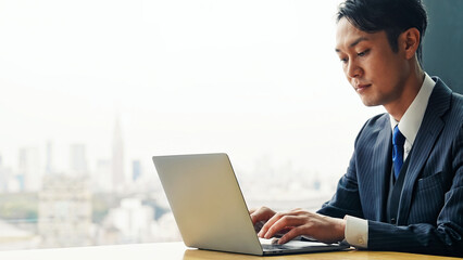 都市のオフィスビルでノートパソコンを使う男性ビジネスパーソン