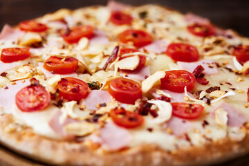 Pizza with ham, cherry tomatoes and mozzarella cheese. Wooden background. Soft focus. Close up.	